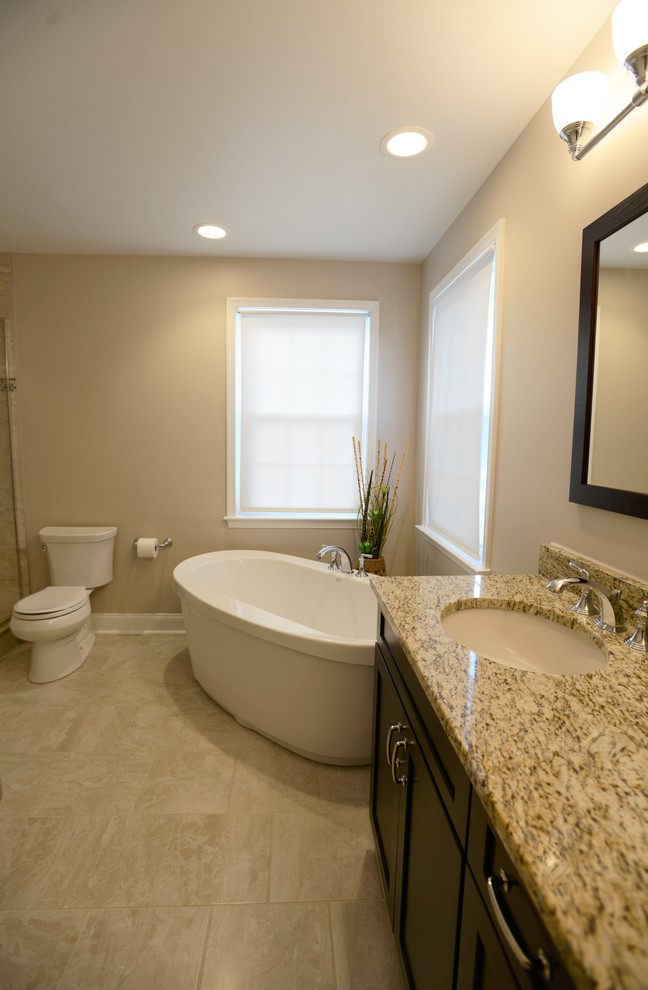 Inspiration for a mid-sized transitional master beige tile and porcelain tile porcelain tile freestanding bathtub remodel in Baltimore with shaker cabinets, dark wood cabinets, a two-piece toilet, beige walls, a drop-in sink and granite countertops