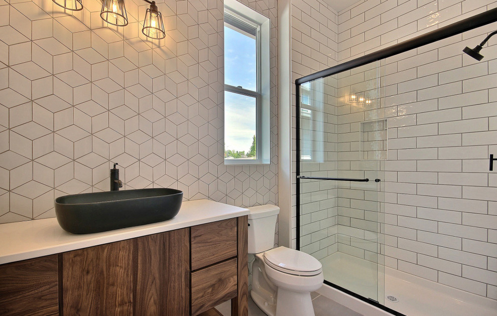 На фото: большая главная ванная комната в стиле модернизм с коричневыми фасадами, душем в нише, унитазом-моноблоком, белой плиткой, керамической плиткой, белыми стенами, полом из керамической плитки, настольной раковиной, столешницей из искусственного кварца, серым полом, душем с раздвижными дверями, белой столешницей и тумбой под одну раковину с