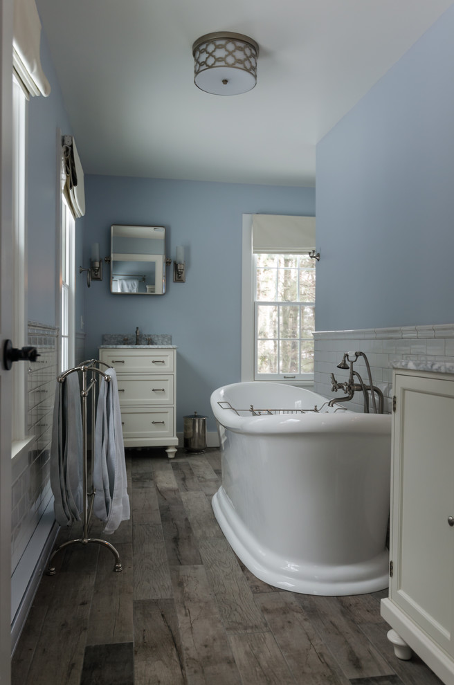 Diseño de cuarto de baño tradicional con armarios estilo shaker, puertas de armario blancas, bañera exenta, paredes azules, suelo de madera oscura, suelo gris y baldosas y/o azulejos azules