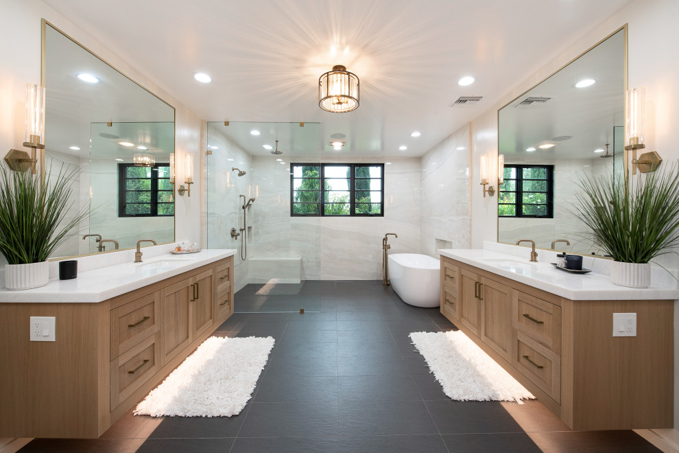 На фото: ванная комната в современном стиле с фасадами в стиле шейкер, фасадами цвета дерева среднего тона, отдельно стоящей ванной, белой плиткой, врезной раковиной, черным полом, белой столешницей, тумбой под две раковины и подвесной тумбой с
