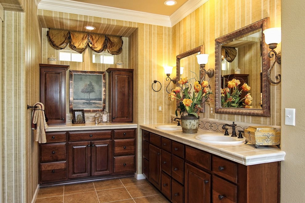 На фото: главная ванная комната в средиземноморском стиле с фасадами с выступающей филенкой, темными деревянными фасадами, бежевой плиткой, каменной плиткой, желтыми стенами, полом из керамогранита, накладной раковиной, столешницей из плитки и бежевым полом