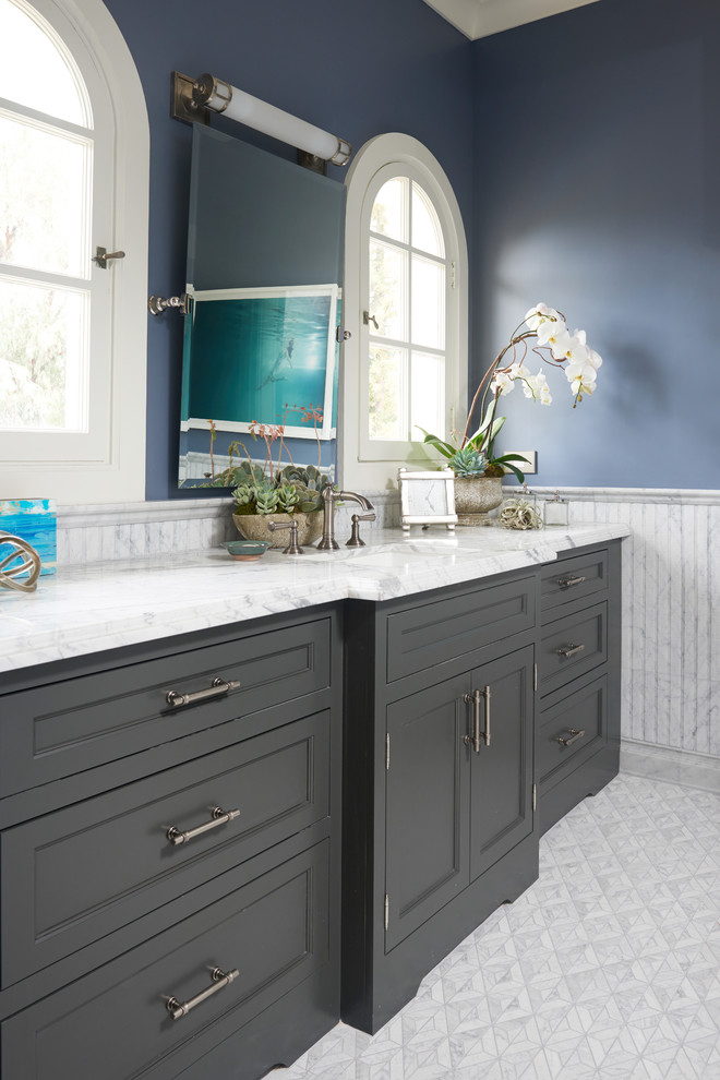 Modelo de cuarto de baño principal tradicional con puertas de armario grises, baldosas y/o azulejos grises, baldosas y/o azulejos de piedra, paredes azules, suelo con mosaicos de baldosas, encimera de mármol, lavabo encastrado y suelo blanco