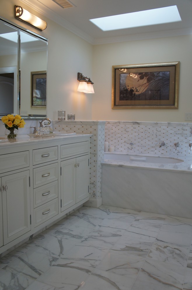 Imagen de cuarto de baño clásico con lavabo bajoencimera, puertas de armario blancas, encimera de cuarcita, bañera encastrada, paredes beige y suelo de mármol