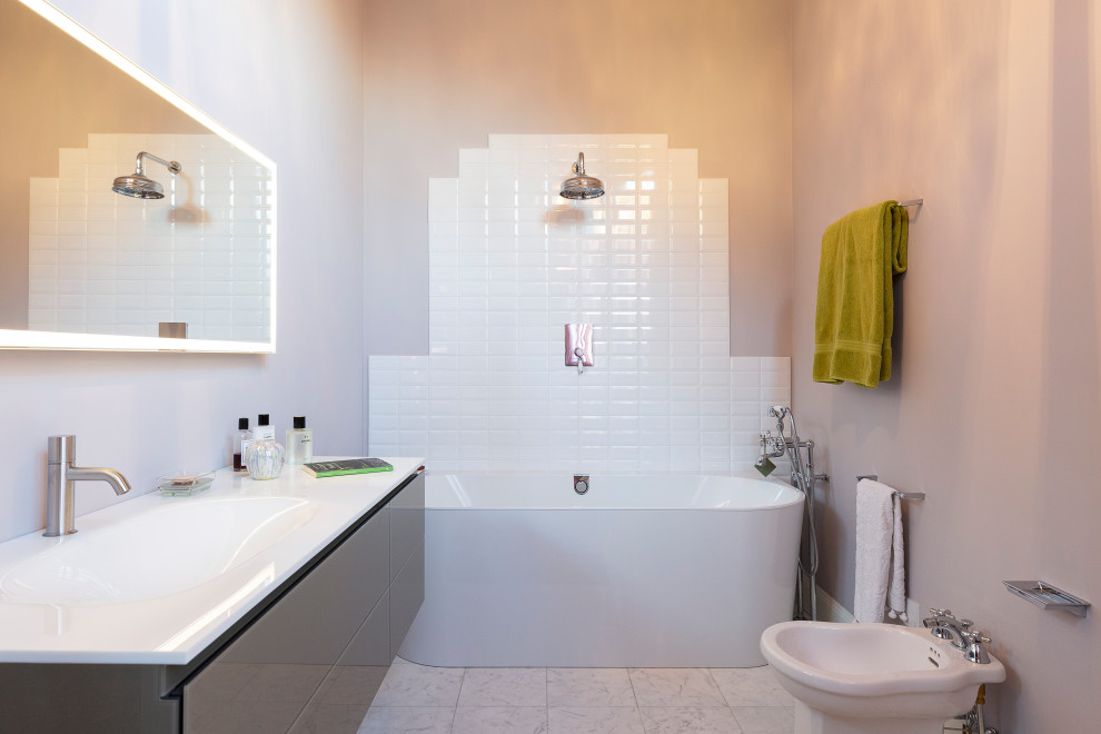 На фото: главная ванная комната среднего размера в стиле модернизм с белой плиткой, розовыми стенами, полом из керамической плитки, стеклянными фасадами, коричневыми фасадами, отдельно стоящей ванной, раздельным унитазом, плиткой кабанчик, накладной раковиной, белой столешницей, тумбой под одну раковину и подвесной тумбой