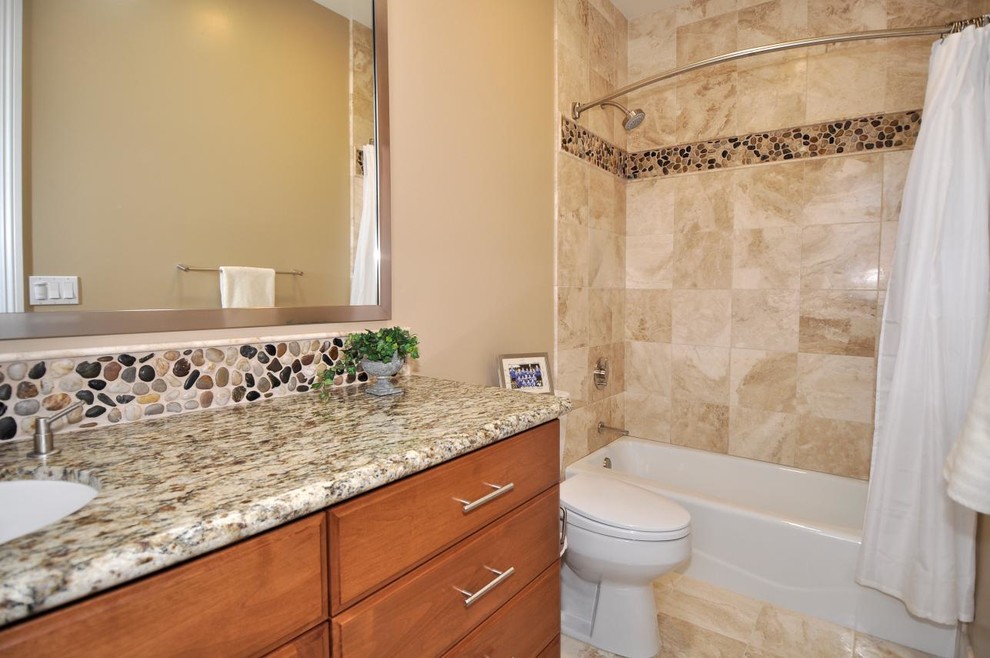 This is an example of a medium sized contemporary shower room bathroom in San Diego with flat-panel cabinets, medium wood cabinets, a shower/bath combination, a two-piece toilet, multi-coloured tiles, pebble tiles, beige walls, travertine flooring, a submerged sink and granite worktops.