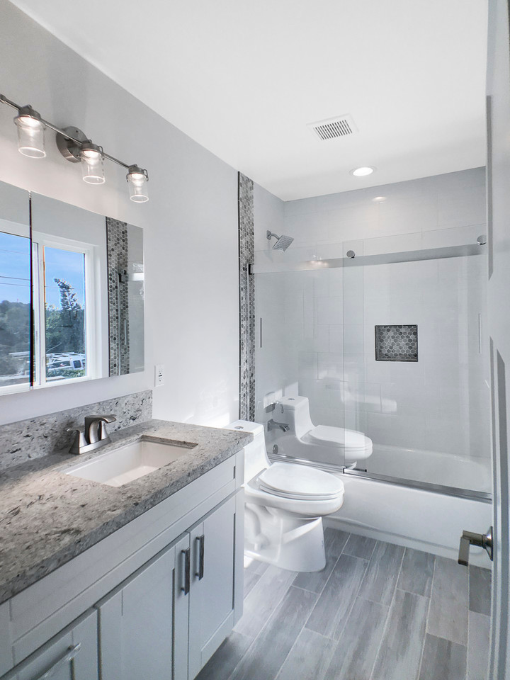 Idéer för att renovera ett mellanstort funkis badrum med dusch, med skåp i shakerstil, vita skåp, ett badkar i en alkov, en dusch/badkar-kombination, en toalettstol med hel cisternkåpa, grå kakel, mosaik, vita väggar, mellanmörkt trägolv, ett undermonterad handfat, granitbänkskiva, grått golv och dusch med skjutdörr