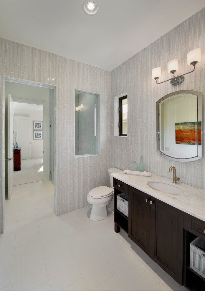 Cette image montre une salle de bain design en bois foncé avec un lavabo encastré, un placard avec porte à panneau encastré, un carrelage gris et un mur gris.