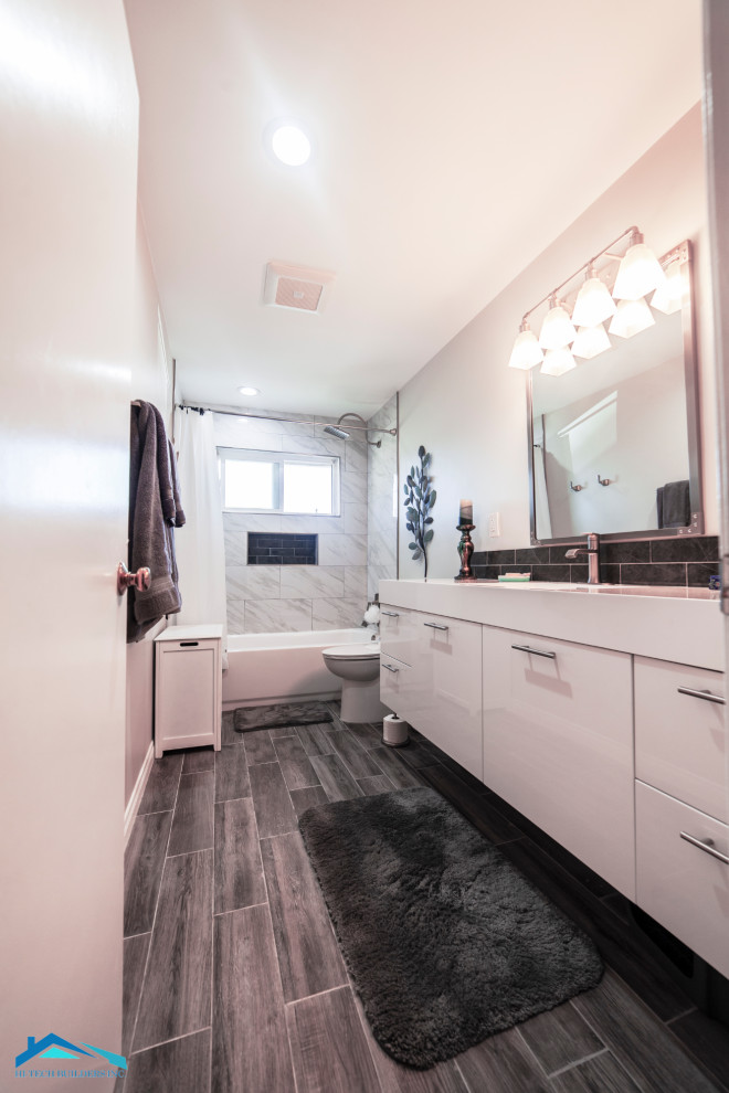 Medium sized modern ensuite bathroom in Los Angeles with flat-panel cabinets, white cabinets, an alcove bath, a shower/bath combination, a two-piece toilet, white tiles, marble tiles, white walls, laminate floors, an integrated sink, solid surface worktops, grey floors, a shower curtain and white worktops.