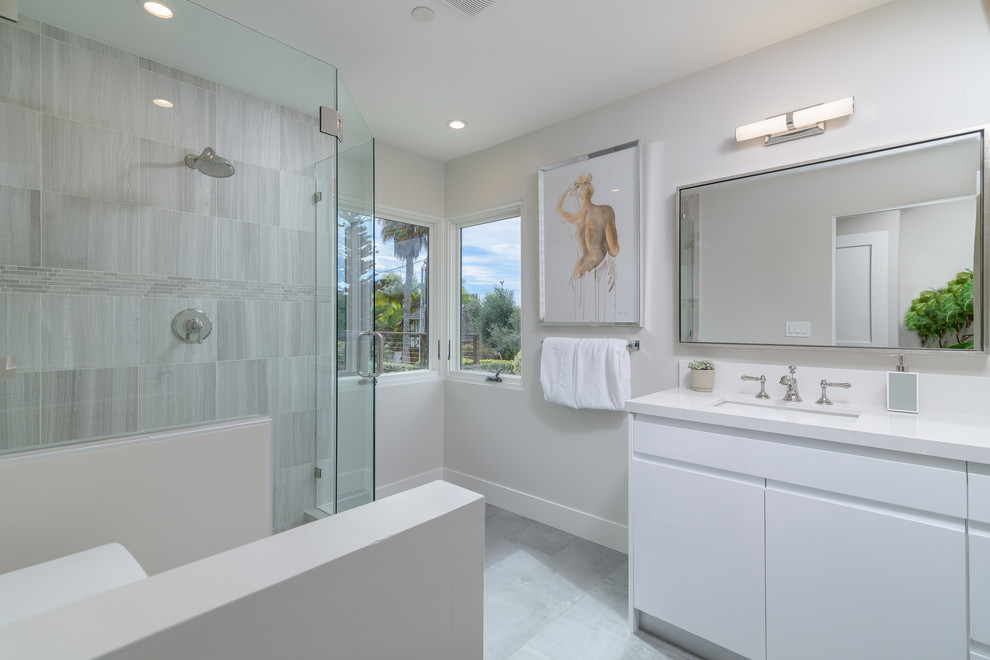 Inspiration for a large modern ensuite bathroom in San Diego with flat-panel cabinets, white cabinets, an alcove shower, a two-piece toilet, beige tiles, ceramic tiles, beige walls, porcelain flooring, a submerged sink, solid surface worktops, grey floors and a hinged door.