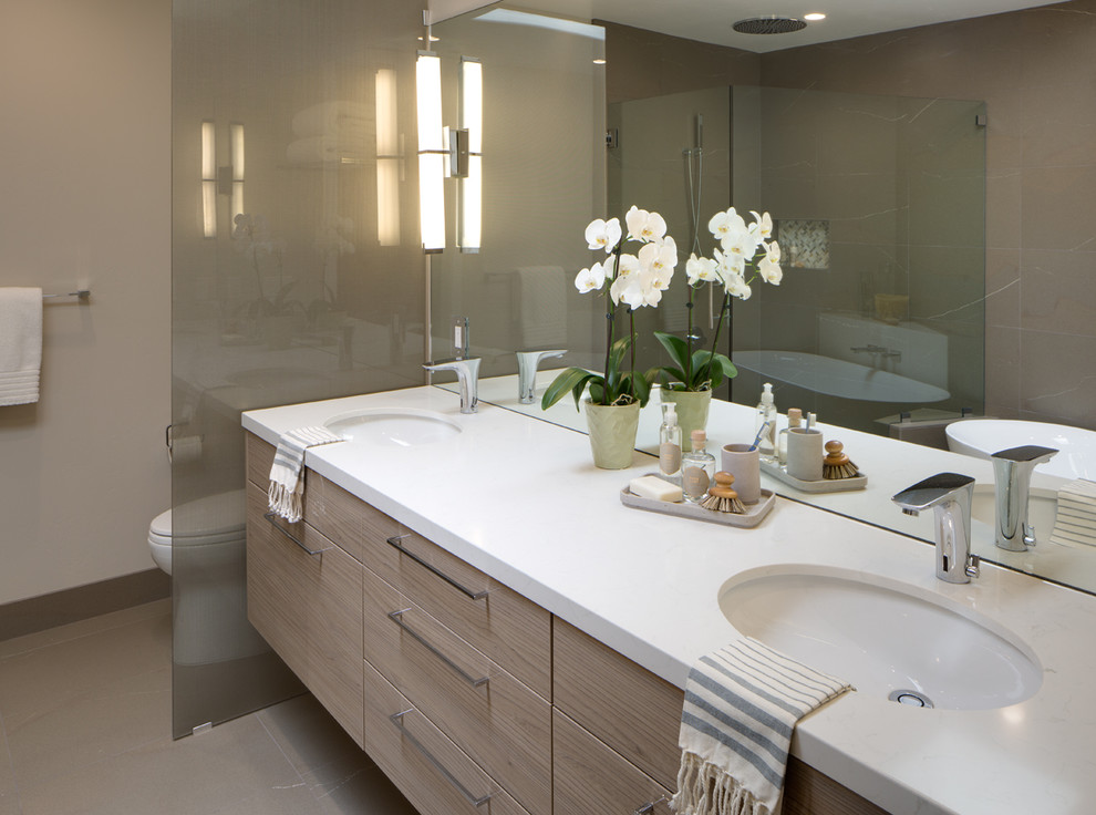 Design ideas for a medium sized contemporary ensuite bathroom in San Diego with a submerged sink, flat-panel cabinets, light wood cabinets, engineered stone worktops, a freestanding bath, a corner shower, a one-piece toilet, grey tiles, porcelain tiles, beige walls and porcelain flooring.