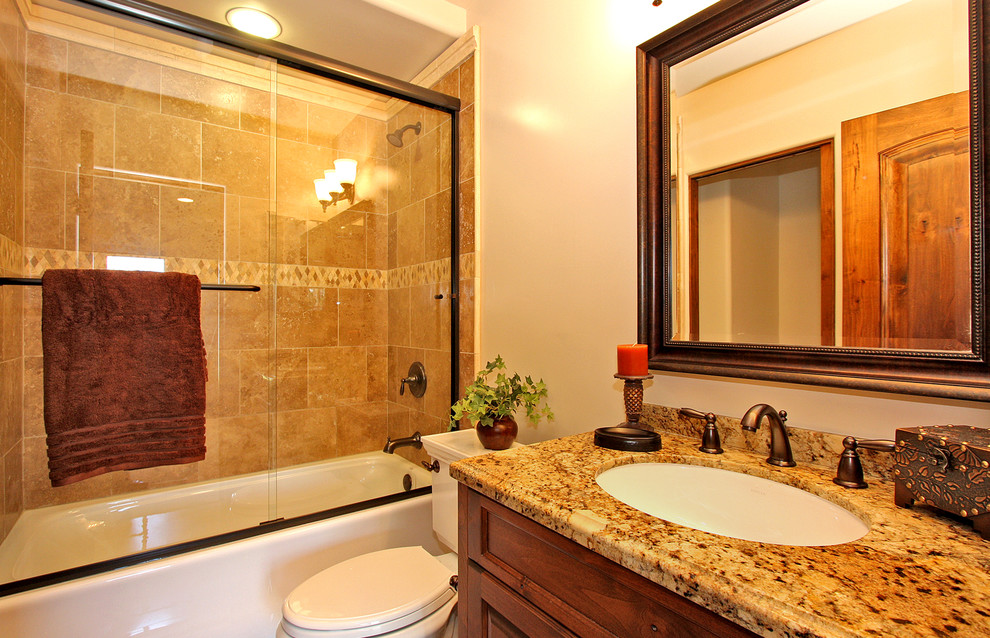 Mid-sized elegant 3/4 beige tile, brown tile and stone slab ceramic tile and brown floor bathroom photo in San Diego with recessed-panel cabinets, medium tone wood cabinets, a two-piece toilet, beige walls, an undermount sink and granite countertops