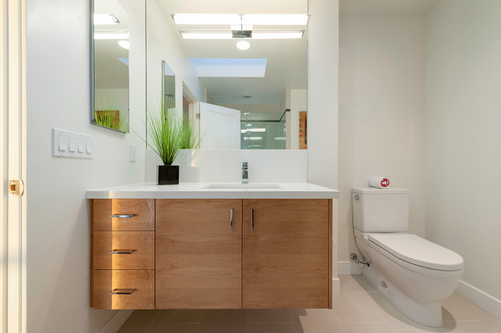 This is an example of a contemporary bathroom in San Diego with a submerged sink, flat-panel cabinets, light wood cabinets, engineered stone worktops, an alcove bath, a walk-in shower, a two-piece toilet, porcelain tiles, white walls and porcelain flooring.