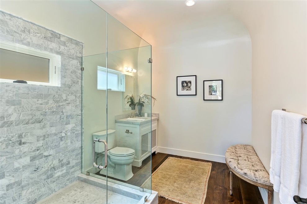 Foto på ett litet medelhavsstil badrum, med ett nedsänkt handfat, möbel-liknande, marmorbänkskiva, en hörndusch, en toalettstol med hel cisternkåpa, grå kakel, cementkakel, vita väggar och mörkt trägolv
