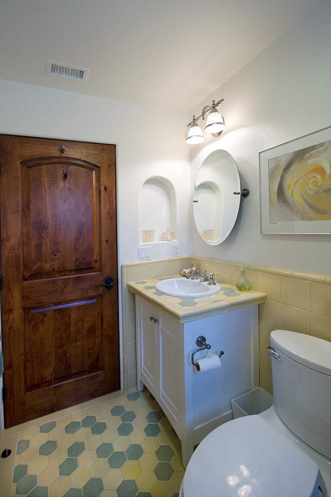 Klassisk inredning av ett litet badrum, med ett nedsänkt handfat, möbel-liknande, vita skåp, kaklad bänkskiva, en toalettstol med separat cisternkåpa, flerfärgad kakel, keramikplattor, vita väggar och klinkergolv i keramik