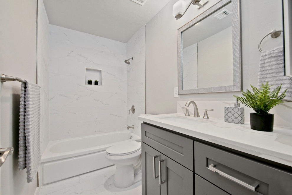 Inspiration för ett mellanstort funkis vit vitt badrum för barn, med skåp i shakerstil, grå skåp, ett badkar i en alkov, en dusch/badkar-kombination, en toalettstol med separat cisternkåpa, vit kakel, stenhäll, grå väggar, klinkergolv i porslin, ett undermonterad handfat, bänkskiva i kvarts, vitt golv och dusch med duschdraperi