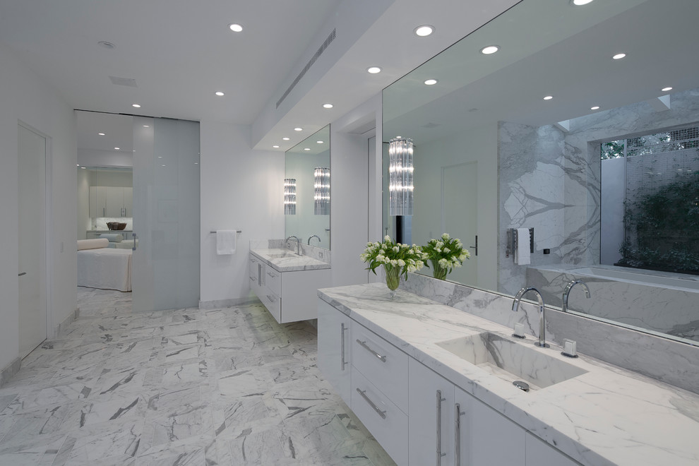Ispirazione per una stanza da bagno padronale minimal di medie dimensioni con ante lisce, ante bianche, vasca ad alcova, piastrelle bianche, lastra di pietra, pareti bianche, pavimento in marmo, lavabo integrato e top in marmo