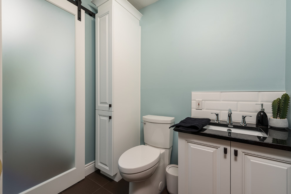 Cette image montre une petite salle de bain traditionnelle pour enfant avec un placard avec porte à panneau surélevé, des portes de placard blanches, WC séparés, un carrelage bleu, un carrelage métro, un mur bleu, un sol en carrelage de porcelaine, un lavabo encastré, un plan de toilette en granite, un sol marron et un plan de toilette noir.