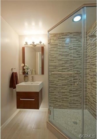 Small trendy master brown tile and ceramic tile light wood floor corner shower photo in Los Angeles with glass-front cabinets, medium tone wood cabinets, solid surface countertops and white walls