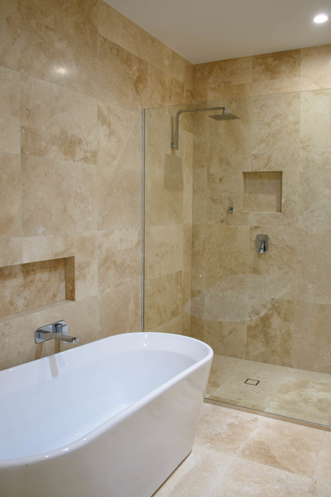 Foto på ett mellanstort maritimt en-suite badrum, med ett fristående badkar, klinkergolv i porslin, marmorbänkskiva, släta luckor, svarta skåp, en dusch i en alkov, travertinkakel, ett integrerad handfat, beiget golv och med dusch som är öppen