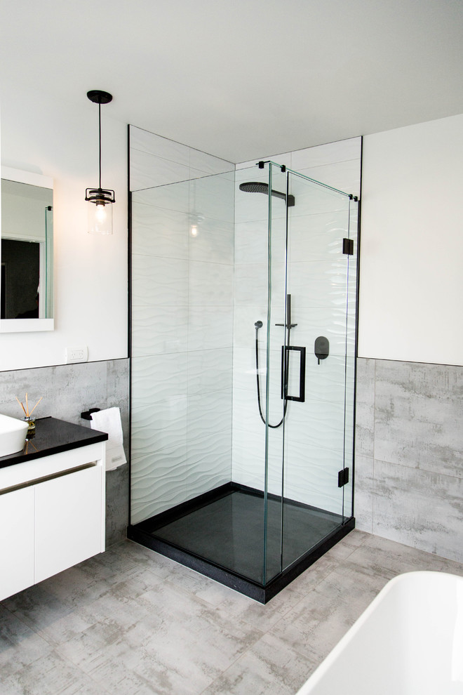 Exempel på ett mellanstort modernt en-suite badrum, med luckor med profilerade fronter, vita skåp, ett fristående badkar, en hörndusch, grå kakel, keramikplattor, vita väggar, klinkergolv i keramik, ett fristående handfat, laminatbänkskiva, grått golv och dusch med gångjärnsdörr