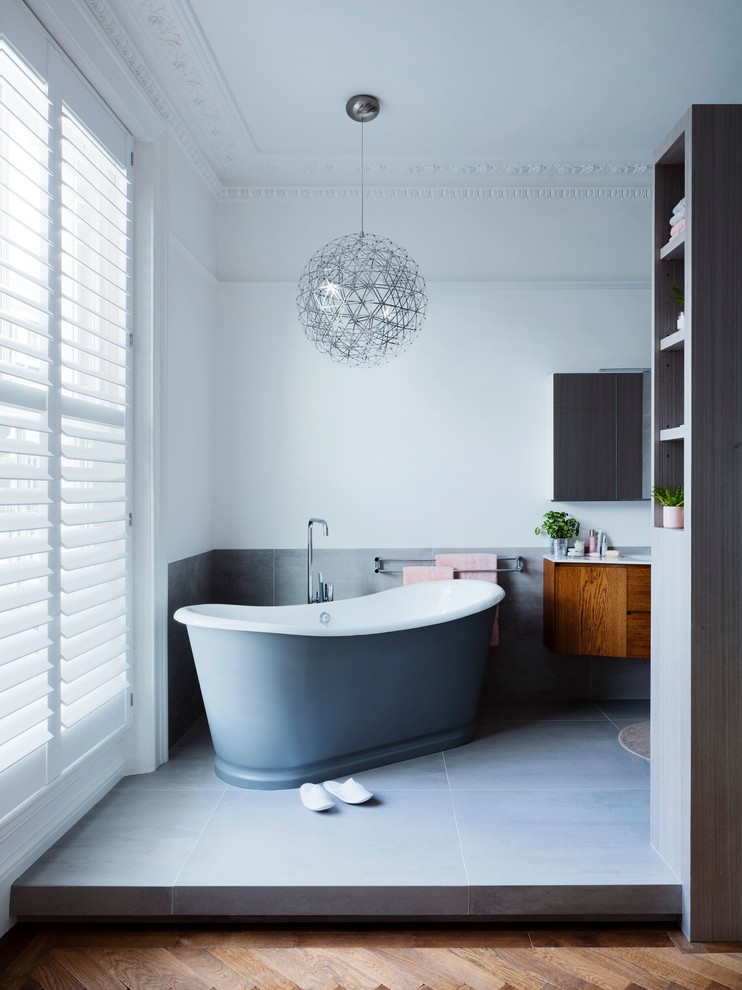This is an example of a large modern ensuite bathroom in London with shaker cabinets, dark wood cabinets, a freestanding bath, a built-in shower, a one-piece toilet, grey tiles, ceramic tiles, white walls, porcelain flooring, a wall-mounted sink, engineered stone worktops, grey floors and a hinged door.