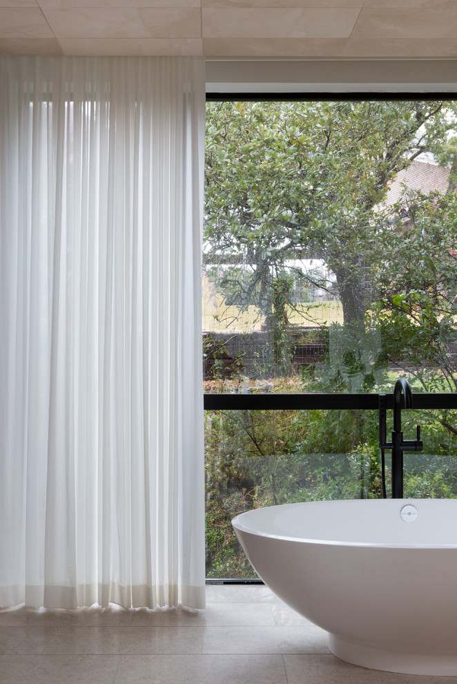 This is an example of a large modern ensuite bathroom in Austin with flat-panel cabinets, light wood cabinets, a freestanding bath, grey tiles, mosaic tiles, beige walls, limestone flooring, a submerged sink, quartz worktops, beige floors and white worktops.