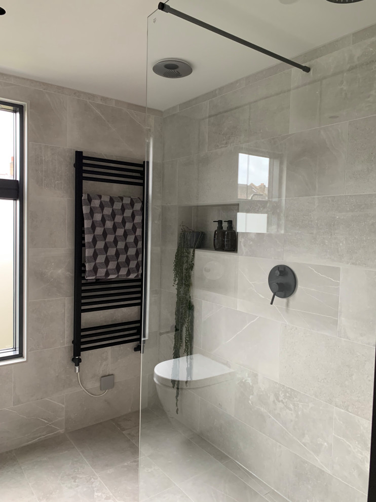Inredning av ett modernt litet grå grått badrum med dusch, med luckor med glaspanel, en öppen dusch, en vägghängd toalettstol, grå kakel, porslinskakel, grå väggar, klinkergolv i porslin, ett nedsänkt handfat, kaklad bänkskiva, grått golv och med dusch som är öppen