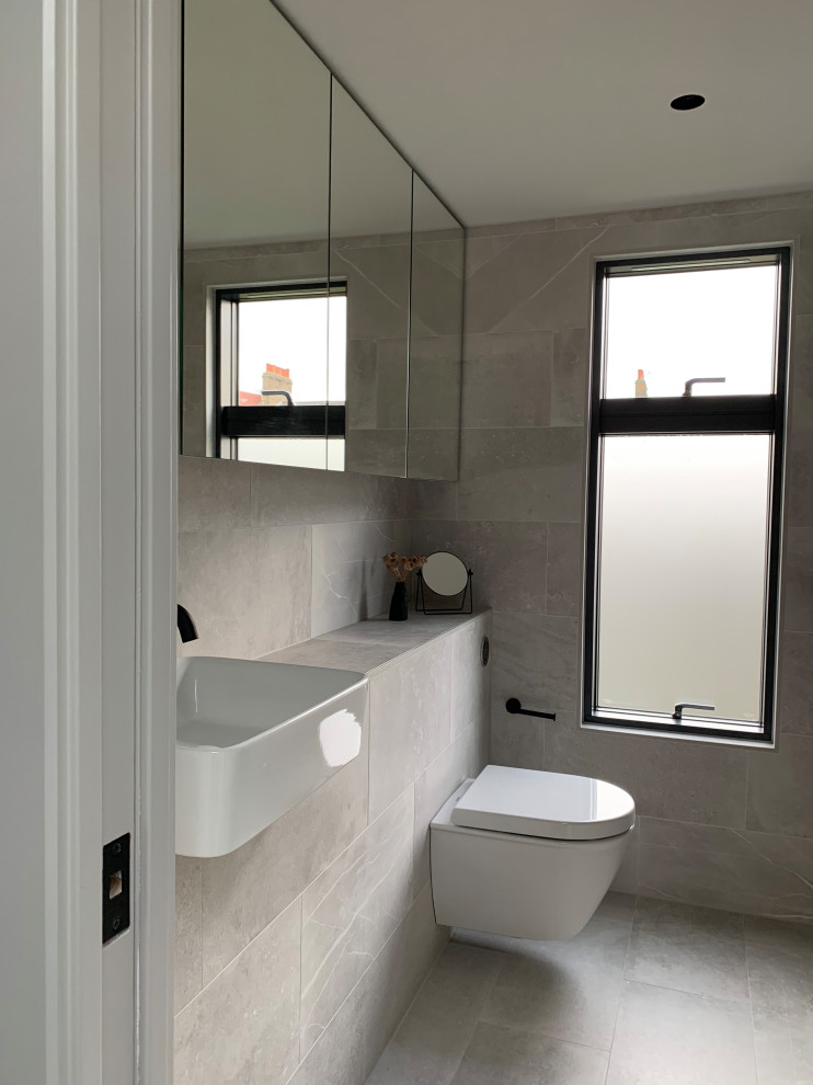 Inredning av ett modernt litet grå grått badrum med dusch, med luckor med glaspanel, en öppen dusch, en vägghängd toalettstol, grå kakel, porslinskakel, grå väggar, klinkergolv i porslin, ett nedsänkt handfat, kaklad bänkskiva, grått golv och med dusch som är öppen