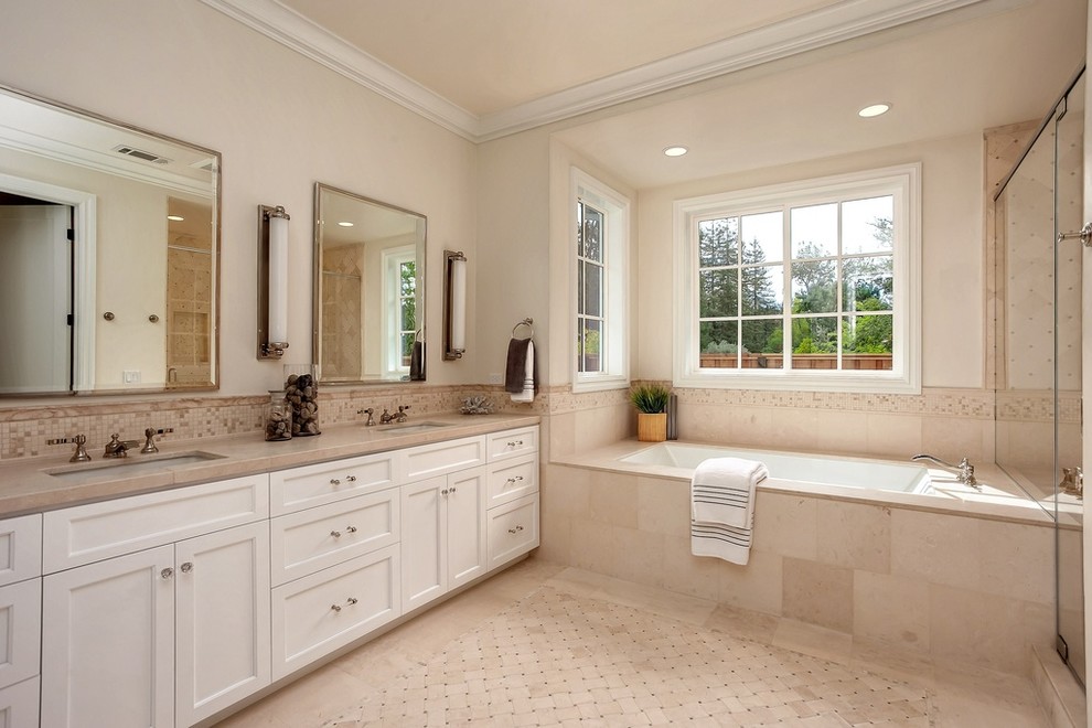 Réalisation d'une salle de bain tradition avec un placard à porte shaker, des portes de placard blanches, une baignoire encastrée, un carrelage beige, un mur beige, un lavabo encastré et une cabine de douche à porte battante.