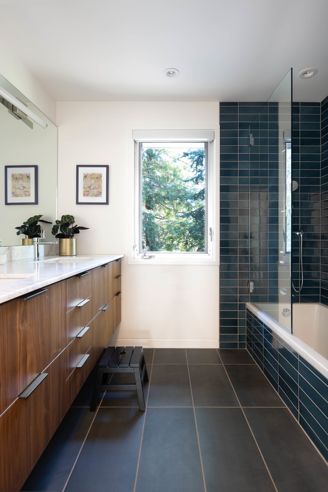 Идея дизайна: ванная комната в стиле ретро с плоскими фасадами, фасадами цвета дерева среднего тона, угловой ванной, душем над ванной, синей плиткой, белыми стенами, врезной раковиной, черным полом, открытым душем и белой столешницей