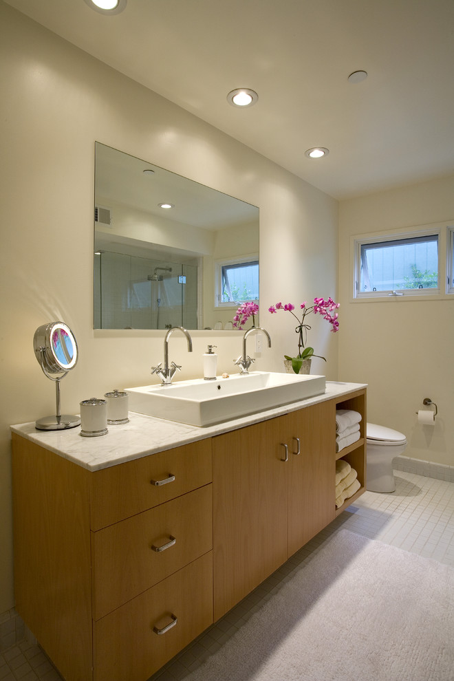 Diseño de cuarto de baño principal retro de tamaño medio con lavabo integrado, armarios con paneles lisos, puertas de armario de madera clara, sanitario de una pieza, baldosas y/o azulejos blancos y paredes beige