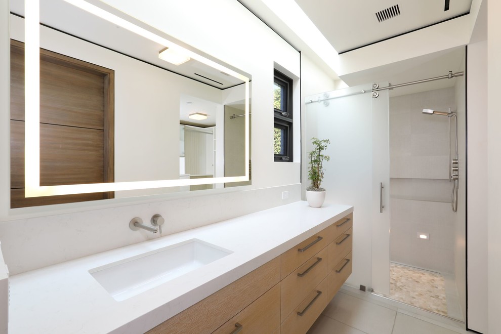 Свежая идея для дизайна: ванная комната в современном стиле с плоскими фасадами, фасадами цвета дерева среднего тона, душем в нише, серой плиткой, белыми стенами, душевой кабиной, врезной раковиной, серым полом, душем с раздвижными дверями, белой столешницей и зеркалом с подсветкой - отличное фото интерьера