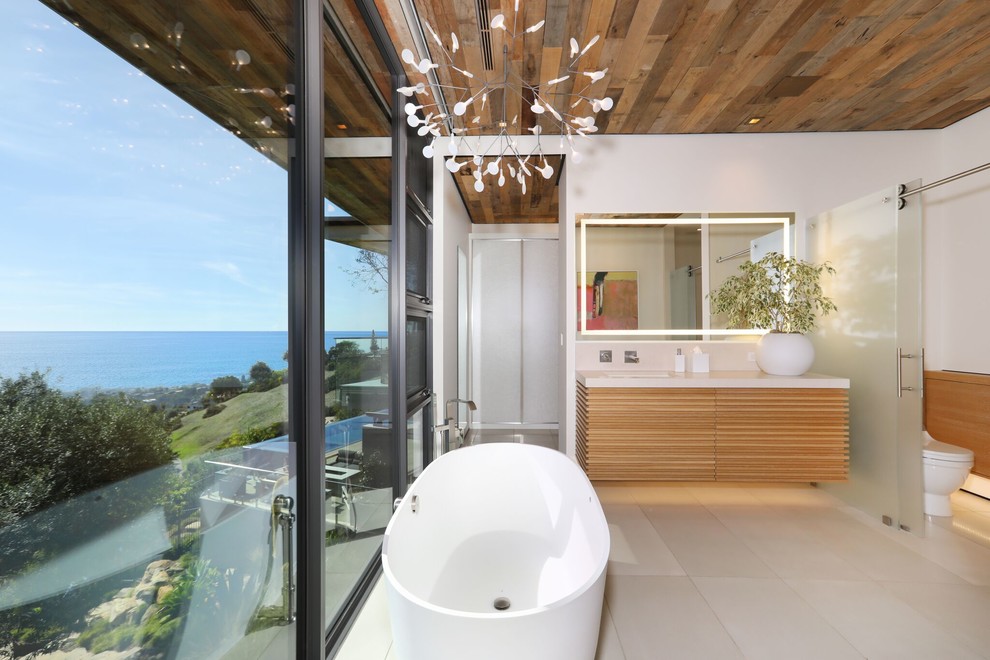 Inspiration for a large contemporary ensuite bathroom in Orange County with light wood cabinets, a freestanding bath, a walk-in shower, a one-piece toilet, white walls, porcelain flooring, solid surface worktops, beige floors, white worktops and flat-panel cabinets.