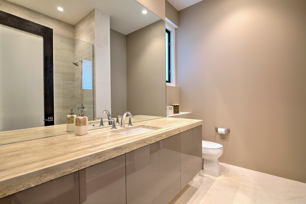 На фото: большая главная ванная комната в стиле неоклассика (современная классика) с плоскими фасадами, коричневыми фасадами, унитазом-моноблоком, коричневыми стенами, полом из известняка и врезной раковиной с