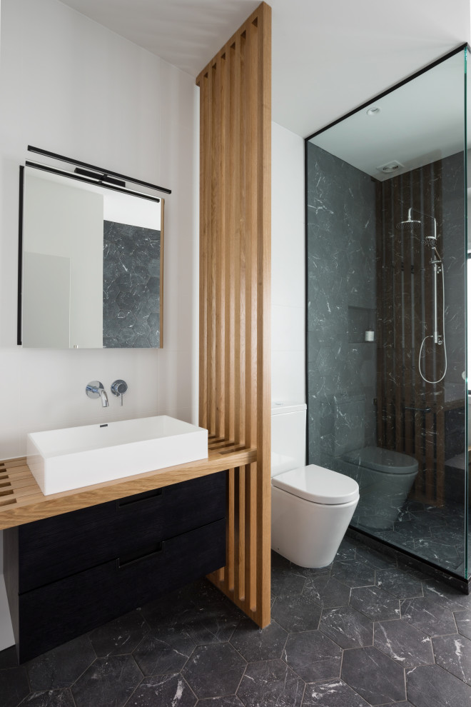 Medium sized contemporary shower room bathroom in Auckland with a corner shower, a one-piece toilet, black tiles, marble tiles, white walls, a vessel sink, wooden worktops, black floors, black cabinets, marble flooring and a single sink.