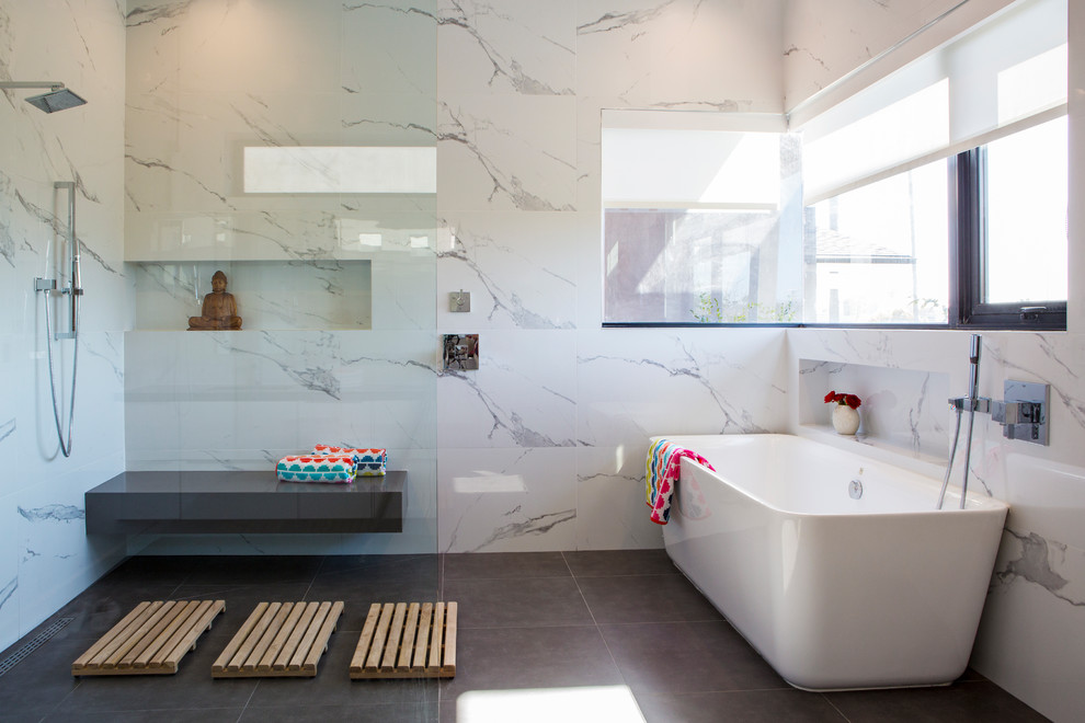 Large contemporary ensuite bathroom in Los Angeles with flat-panel cabinets, white cabinets, a freestanding bath, a shower/bath combination, white tiles, marble tiles, white walls, porcelain flooring, a submerged sink, solid surface worktops, grey floors, an open shower and black worktops.