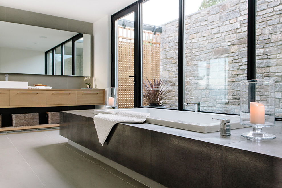Photo of a modern ensuite bathroom in Vancouver with flat-panel cabinets, brown cabinets, a built-in bath, grey walls, concrete flooring, wooden worktops and grey floors.