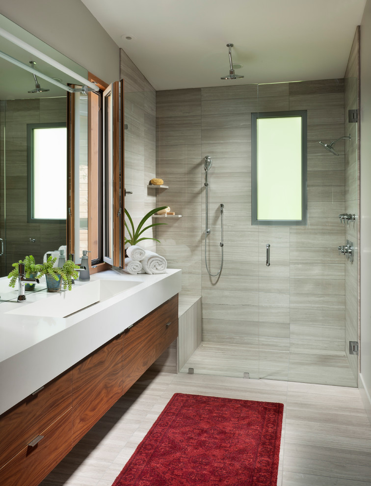 Ejemplo de cuarto de baño actual con armarios con paneles lisos, puertas de armario de madera oscura, ducha empotrada, baldosas y/o azulejos grises, paredes grises, lavabo integrado y ventanas