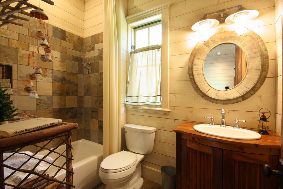 Cette image montre une petite salle d'eau chalet en bois brun avec un lavabo posé, un plan de toilette en bois, du carrelage en ardoise, un plan de toilette marron, un placard avec porte à panneau encastré, une baignoire en alcôve, un combiné douche/baignoire, WC séparés, un carrelage marron, un mur beige et une cabine de douche avec un rideau.