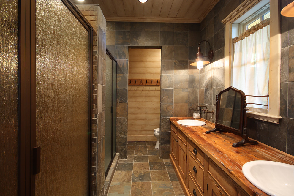 Idéer för ett litet rustikt brun en-suite badrum, med ett nedsänkt handfat, en dusch i en alkov, skifferkakel, luckor med infälld panel, skåp i mellenmörkt trä, en toalettstol med hel cisternkåpa, brun kakel, bruna väggar, skiffergolv, träbänkskiva, brunt golv och dusch med gångjärnsdörr