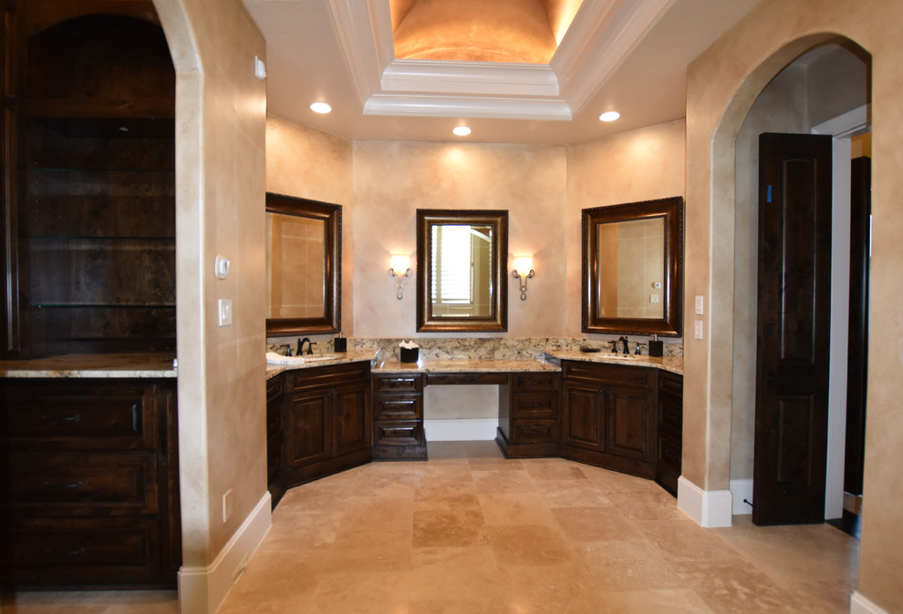 Пример оригинального дизайна: большая главная ванная комната в средиземноморском стиле с фасадами с выступающей филенкой, темными деревянными фасадами, полновстраиваемой ванной, душем в нише, раздельным унитазом, бежевой плиткой, каменной плиткой, полом из травертина, врезной раковиной и столешницей из гранита