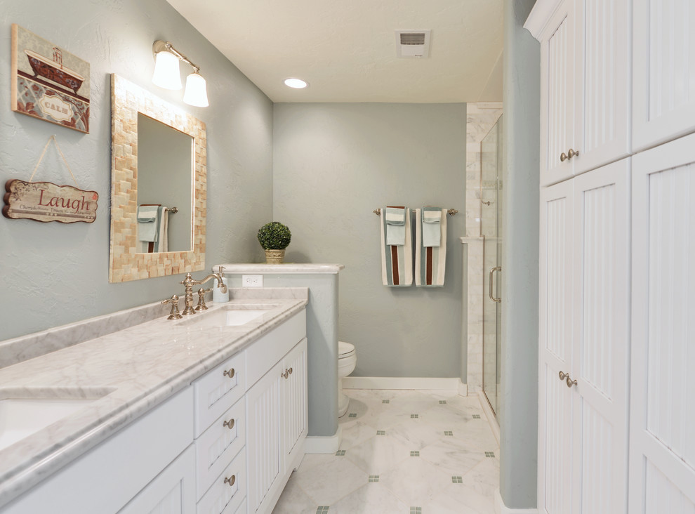 Immagine di una stanza da bagno stile marino con lavabo sottopiano, ante bianche, top in marmo, piastrelle in pietra e pavimento in marmo