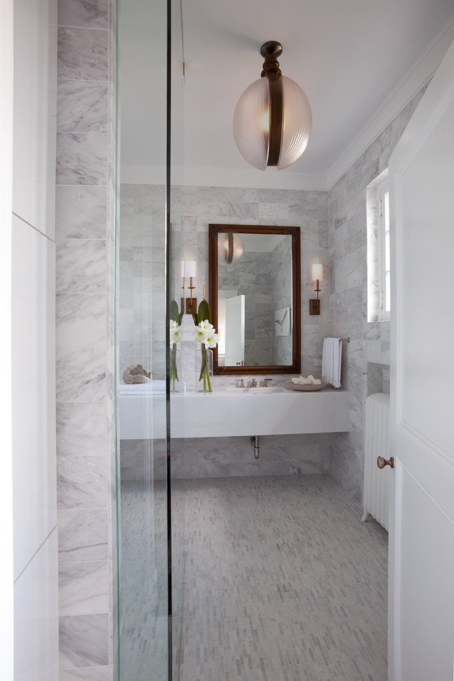 Klassisk inredning av ett litet badrum, med ett integrerad handfat, släta luckor, vita skåp, marmorbänkskiva, en öppen dusch, en toalettstol med hel cisternkåpa, stenkakel, vita väggar, marmorgolv och grå kakel