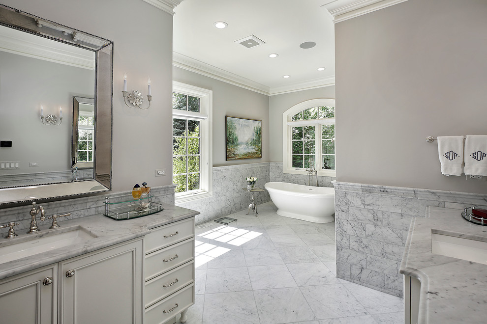 Foto de cuarto de baño principal clásico renovado con armarios con paneles empotrados, puertas de armario grises, bañera exenta, paredes grises y lavabo bajoencimera