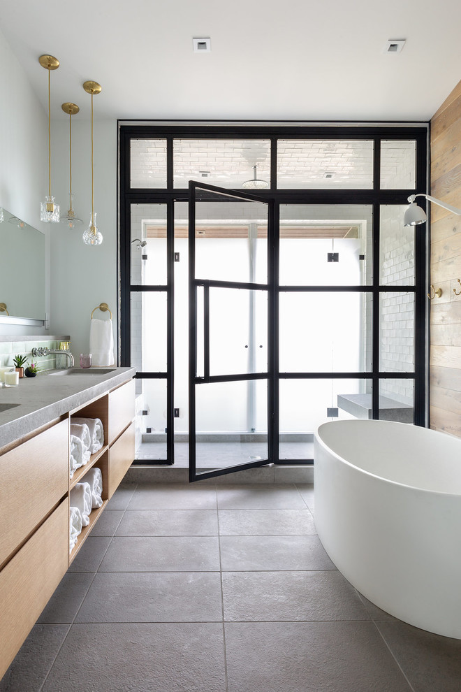 Cette image montre une salle de bain design en bois brun avec un placard à porte plane, une baignoire indépendante, un mur gris, un lavabo encastré, un sol gris et un plan de toilette gris.