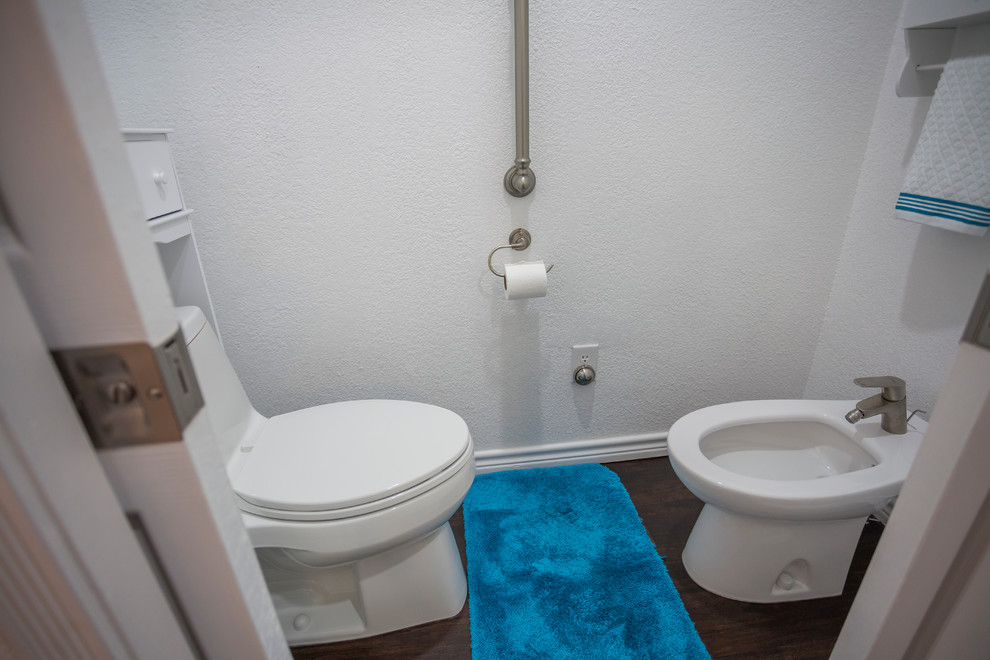 Cette image montre une salle de bain principale traditionnelle de taille moyenne avec un placard à porte shaker, des portes de placard blanches, une douche d'angle, un bidet, un carrelage blanc, des carreaux de céramique, un mur blanc, un sol en vinyl, une vasque et un plan de toilette en quartz modifié.