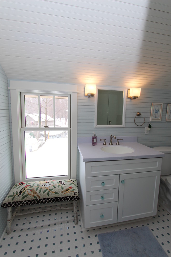 Inredning av ett maritimt badrum med dusch, med vita skåp, en dusch i en alkov, klinkergolv i keramik, ett undermonterad handfat, skåp i shakerstil, bänkskiva i akrylsten, en toalettstol med separat cisternkåpa, flerfärgad kakel, keramikplattor och blå väggar