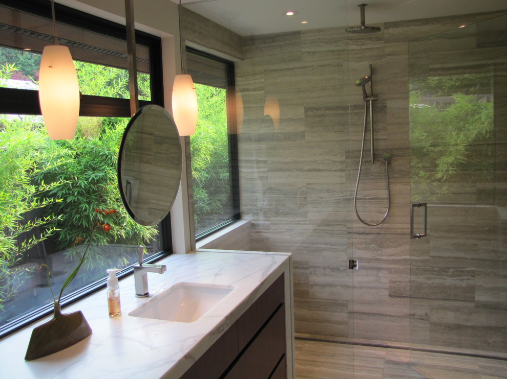 Exempel på ett mycket stort modernt badrum med dusch, med släta luckor, skåp i mellenmörkt trä, en kantlös dusch, travertinkakel, travertin golv, ett undermonterad handfat, marmorbänkskiva och dusch med gångjärnsdörr
