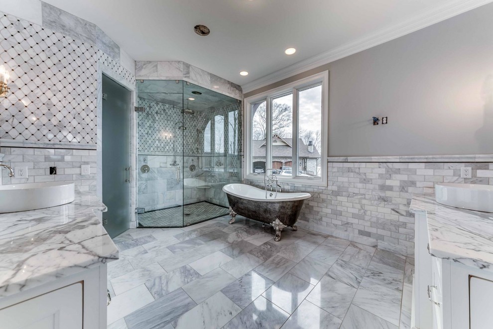 Klassisk inredning av ett stort en-suite badrum, med luckor med infälld panel, vita skåp, ett fristående badkar, en toalettstol med separat cisternkåpa, vit kakel, stenkakel, grå väggar, klinkergolv i porslin, ett fristående handfat, marmorbänkskiva, vitt golv, dusch med gångjärnsdörr och en dubbeldusch