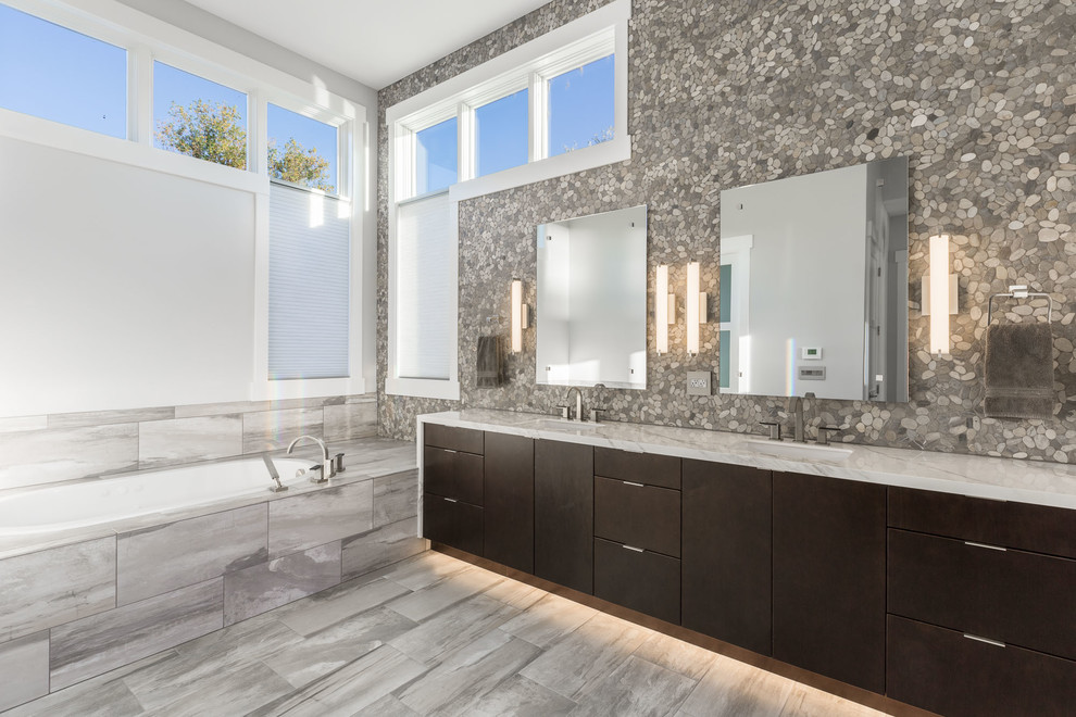 Cette image montre une salle de bain design en bois foncé avec un placard à porte plane, une baignoire posée, une plaque de galets et un lavabo encastré.